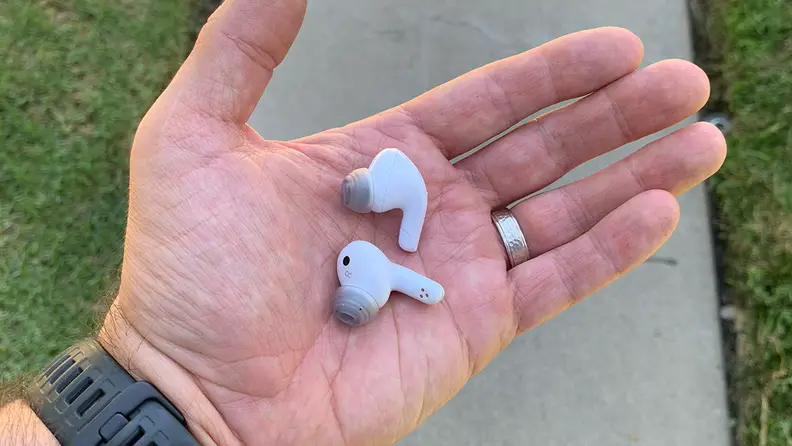 The LG T90Q earbuds in a man's hand with a walkway and grass in the background.