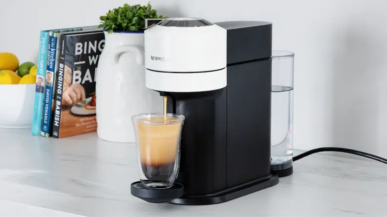 Nespresso Vertuo Next coffee maker on marble countertop next to potted plant and kitchen utensils.