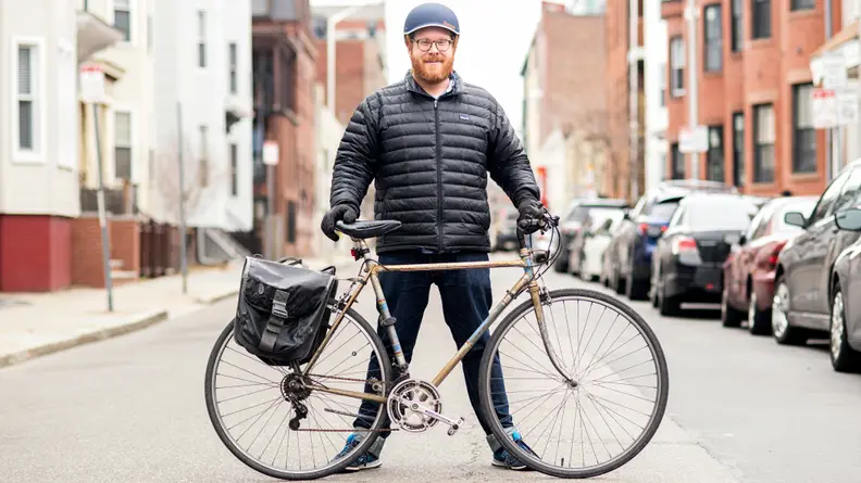 A man standing behind his bicycle in the road.