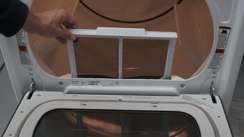 A hand reaches into frame, pulling up the lint trap slightly.