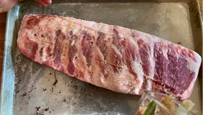 An uncooked rack of ribs rests on a parchment-lined sheet pan.