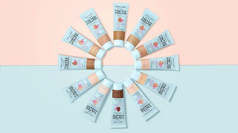 A circle of 12 Wet n Wild Bare Focus Tinted Hydrators on a blue and pink background.