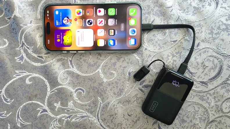iPhone shown plugged into the INIU Pocket Rocket 50 portable charger on a shiny grey patterned cloth.
