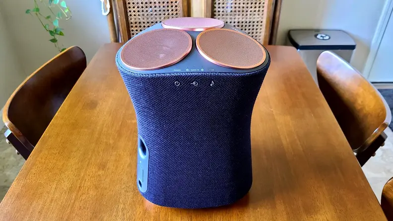 Sony SRS-RA5000 sits on a wooden kitchen table, its hour-glass shape lit with sunlight and revealing its controls