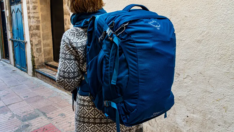 A person wearing a fully loaded Osprey travel backpack.