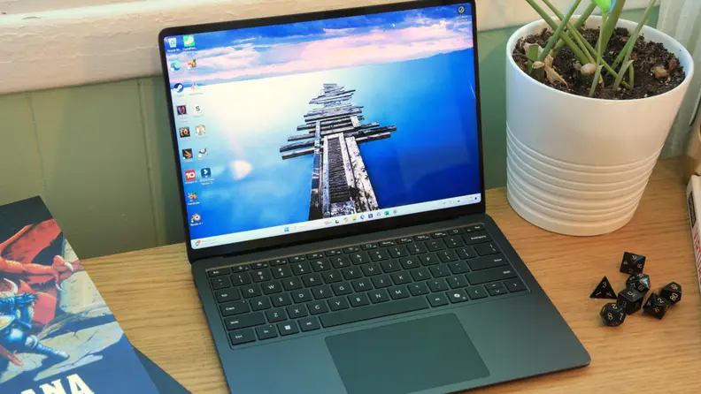 An opened Microsoft Surface Laptop 7th Edition on a desk next to a potted plant and dice.