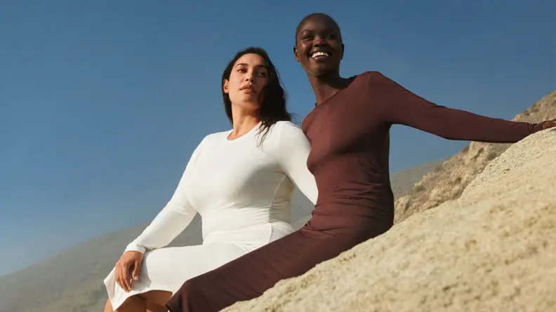 Two women sitting in the sand in dresses