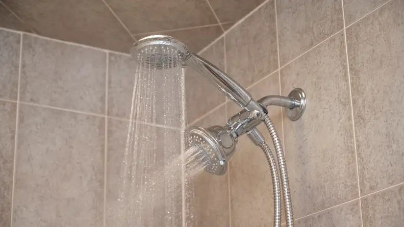 The Hydroluxe Full Chrome shower head, our tester's favorite shower head, spraying water from both the shower head and sprayer attachment, in a tiled shower stall.