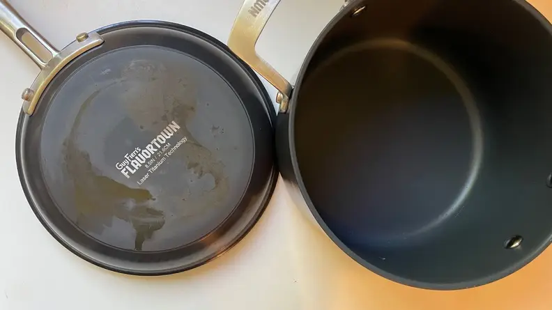 A discolored, worn bottom of the Guy Fieri Flavortown Laser Titanium skillet and the empty inside of a pot.