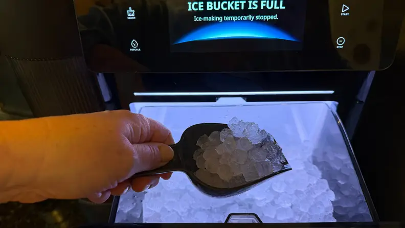 A person scooping nugget ice from the bin while the machine display indicates the ice bucket is full.