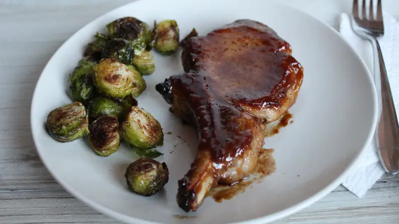 On a plate , there's the Snake River Farm pork chops accompanied by cooked Brussels sprouts and a fork.