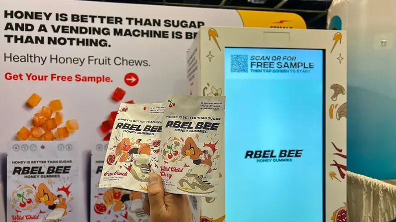 Hand holding two Rbel Bee packets in front of a display