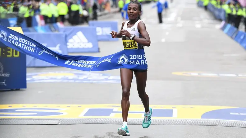 Worknesh Degefa running across the finish line at the 2019 Boston Marathon in first place, wearing a pair of Adidas adiZero Adios Boost 3.