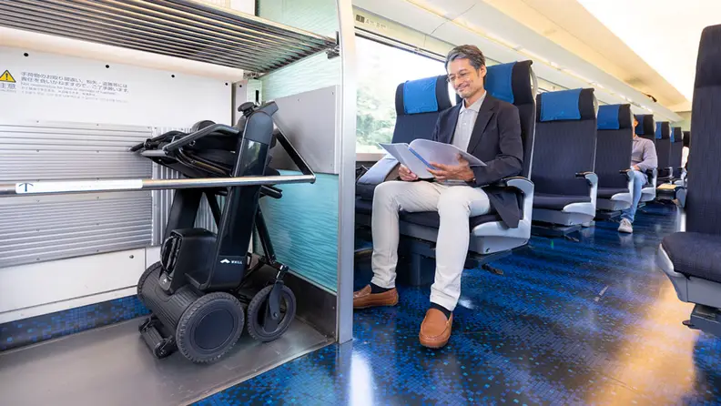 A person rides a train with their wheelchair folded on the side.