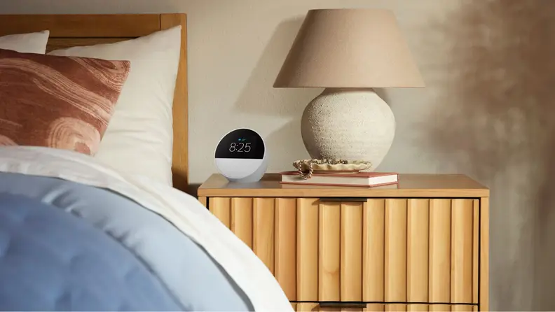 An Amazon Echo Spot smart alarm clock in white sitting on a light wood nightstand in a bedroom