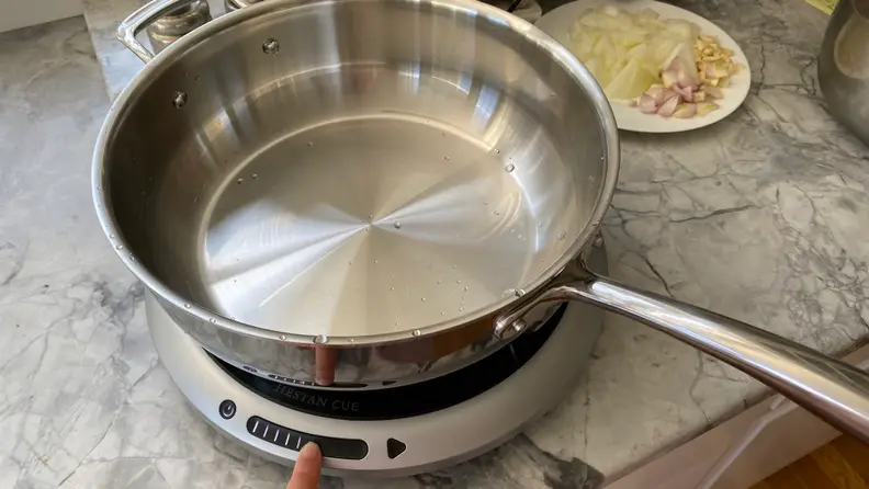 The stainless steel Hestan Cue 5.5-quart Chef's Pot is sitting on top of the Hestan Cue induction hot plate on a kitchen counter.