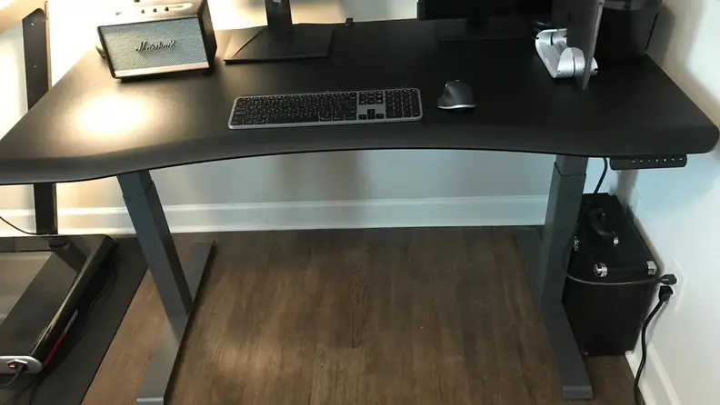 A computer desk with two monitors, a speaker, and keyboard in a living room.