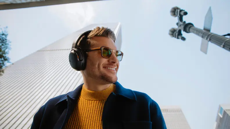 A model in sunglasses and winterwear sports a set of JBL Tour One noise-canceling headphones.