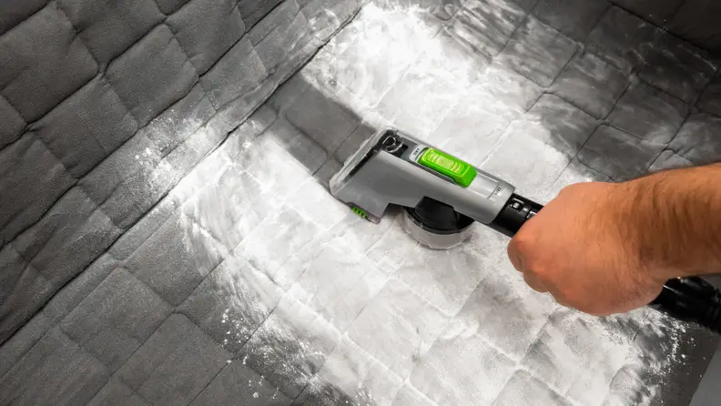 A person vacuums a patch of baby powder off a car seat