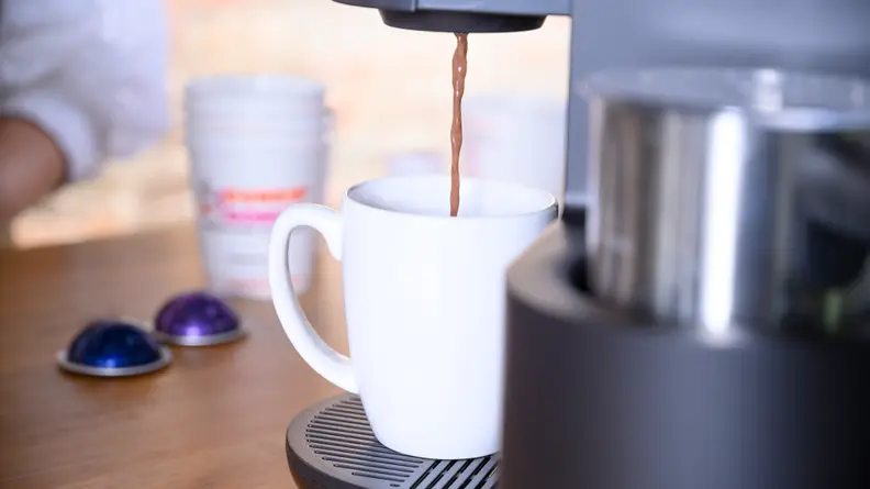 A white mug of coffee under a Keurig coffee maker