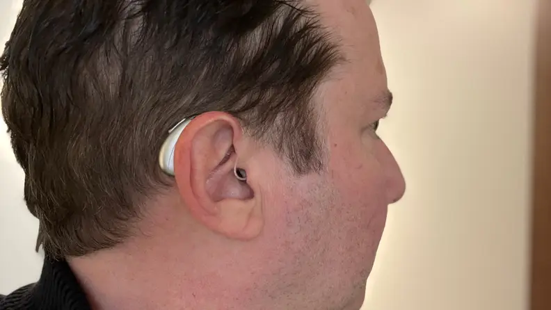 A hearing aid sits behind a man's ear as he gazes in profile