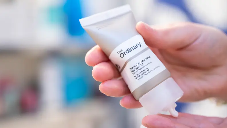 A person's hands squeezing face moisturizer from a gray tube.