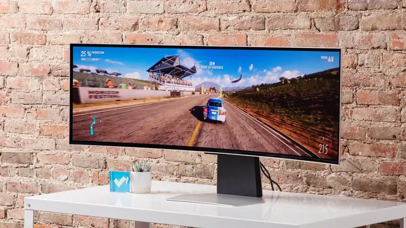 The Samsung’s Odyssey OLED G9 on a white table with a brick background.