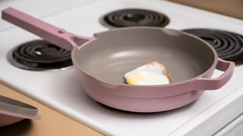 A lavender colored Always Pan is on a white stovetop with a fried egg in it.