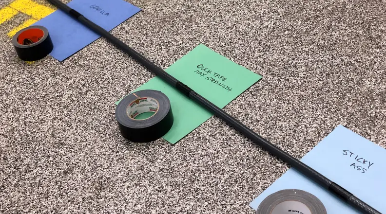 A length of garden hose. Tape is wrapped around the hose at regular intervals. A labeled placard sits under each piece of tape, identifying each one for waterproof testing.