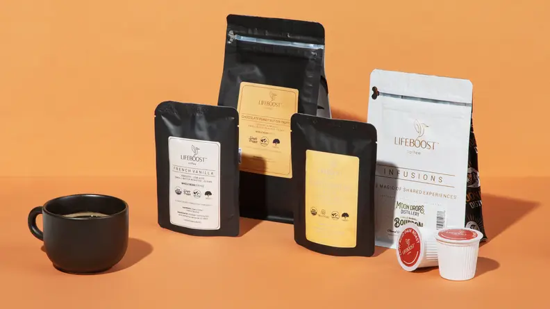 A black cup of coffee next to four bags of Lifeboost Coffee and products.