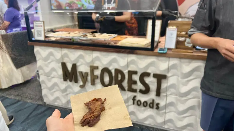 Hand holding plant-based bacon in front of Expo West display