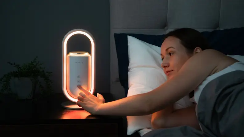 A person in bed reaches over to press a button on their Aromeo Sense wellness device.
