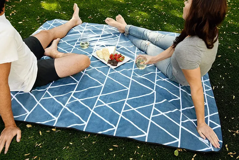 Two people sitting on a blue outdoor blanket on grass.
