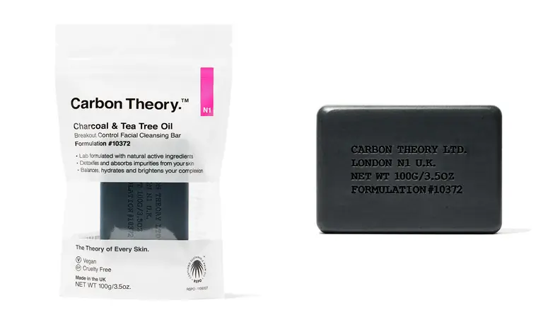 On the left: The Carbon Theory Charcoal & Tea Tree Oil Break-Out Control Facial Cleansing Bar inside its packaging sits on a white background. On the right: The dark gray Carbon Theory Charcoal & Tea Tree Oil Break-Out Control Facial Cleansing Bar sits on a white background. it has words imprinted on to it.