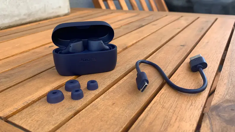 The Jabra Elite 4 earbuds outside a black and next to a black USB cord on a table.