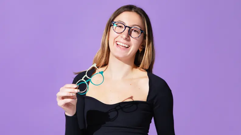 Woman wearing black shirt and smiling in pair of eyeglasses in front of purple background