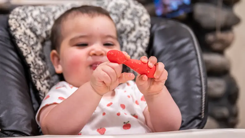 A baby sitting in a high chair holding a red spoon.