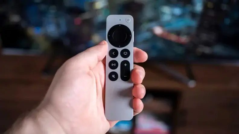The Apple TV 4K remote in someone's hand in front of a television.