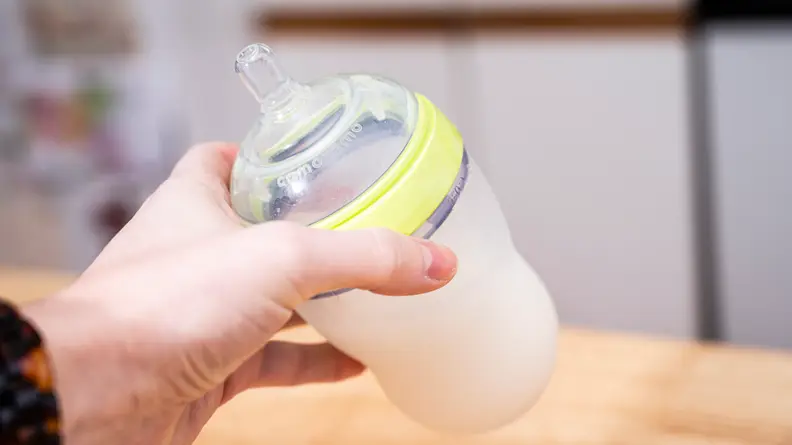 The Comotomo baby bottle full of milk or formula, being held by a hand.