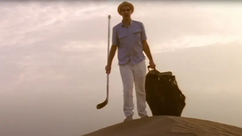 A man walking in the desert with a bag and a hockey stick