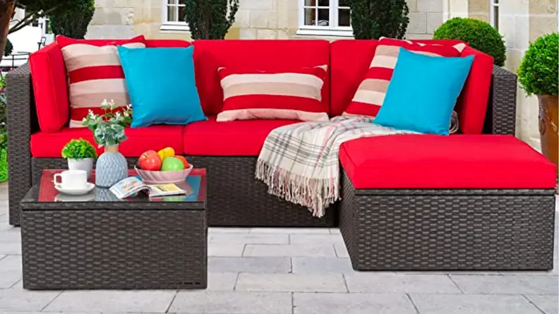 An image of a red-cushioned sectional three-seater sofa with an extended ottoman, next to a brown wicker coffee table.