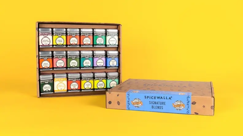An assortment of spice tins arranged in a cardboard box against a bright yellow background.
