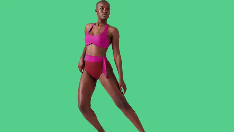 Black woman wearing pink bikini on green background.