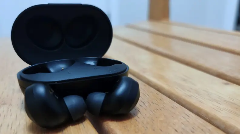 The all-black Raycon Everyday Earbuds sitting in front of their black charging case on light wooden slats.
