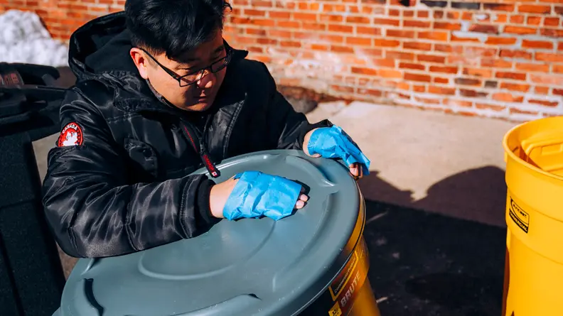 Tester with brown hair and glasses trying to open a trash can with his hands taped up to simulate an animal's paw.