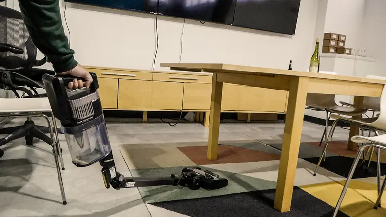 The Shark Stratos cordless vacuum squeezes under a wooden table to clean the floor beneath it.
