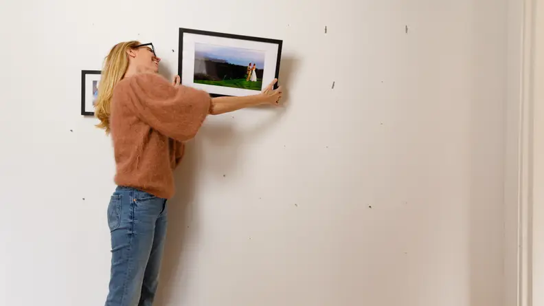 A woman hangs a photo on a wall