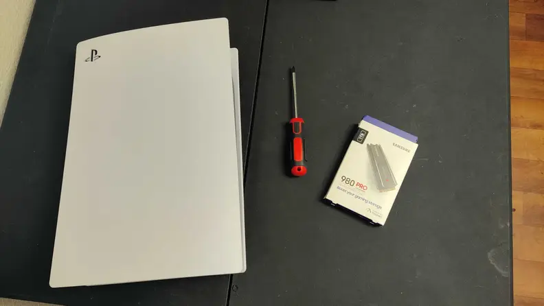The Sony Playstation 5, a #1 Phillips screwdriver and the packeging for the Samsung 980 Pro sitting on a table.