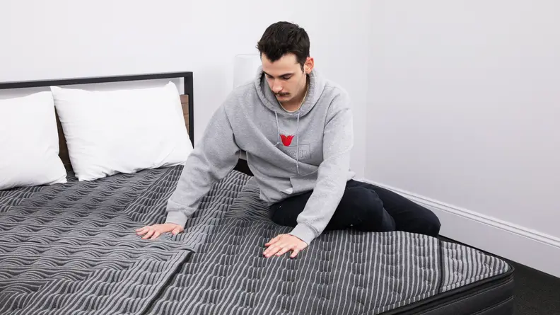 The mattress's tester sitting on the edge of the mattress and pressing down on the center.