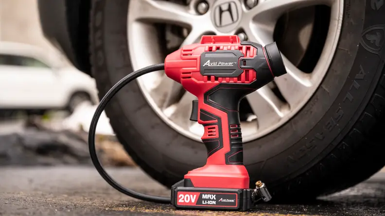The Avid Power 10v portable tire inflator sits next to the front tire of a car.